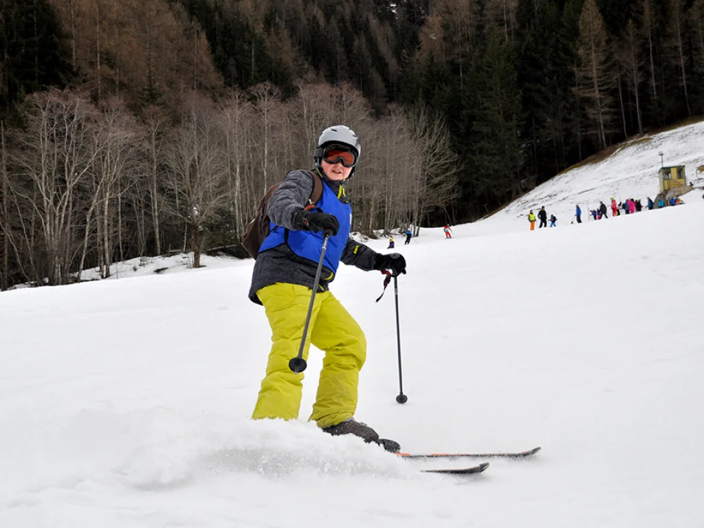 Skifahrer in gelber Hose bremst mit aufstiebendem Schnee.